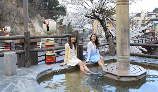 周囲にこけしが立ち並ぶ土湯温泉の足湯を楽しむ女性達