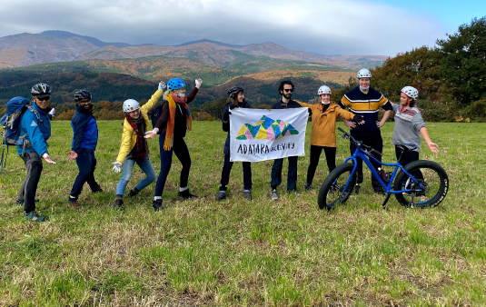 安達太良山を背景に高原で写真撮影をするヘルメット姿の人々